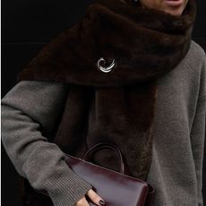 Woman in a gray sweater, brown faux-fur scarf, and burgundy bag