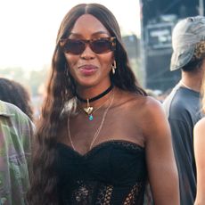 Naomi wears sunglasses, a black choker necklace, and black strapless top.