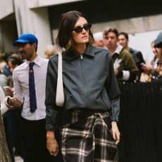A woman wearing a gray jacket, white bag, and plaid skirt at London Fashion Week
