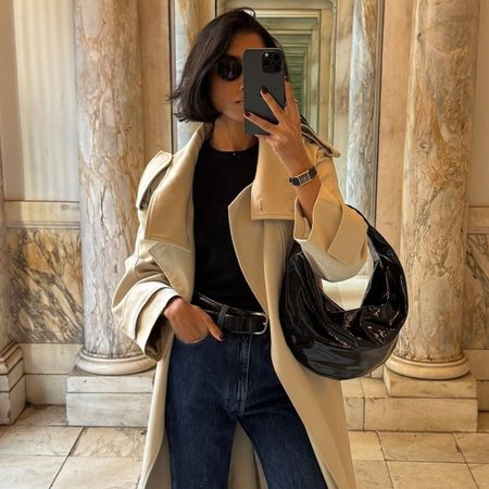 Shay wears a trench coat, black tank, belt, jeans, and a khaite bag.