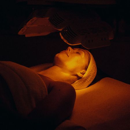 An up-close shot of a bottled skincare product and an image of a woman getting a facial in a dark room.
