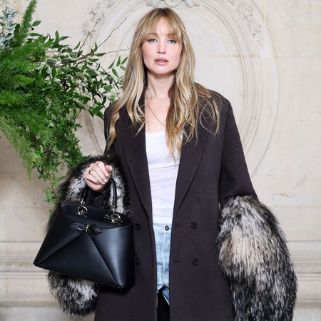 Jennifer Lawrence poses for a photo wearing puddle jeans with pointed-toe heels and a black tailored coat.