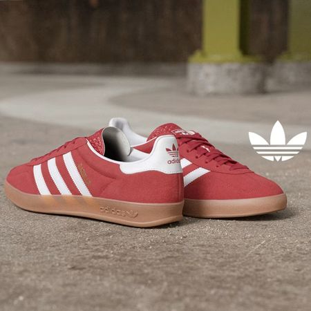 Red Adidas Gazelle sneakers on a concrete road with the Adidas logo next to them